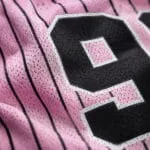 Custom pink baseball T-shirt fabric close-up showing breathable mesh texture, black pinstripes and number print