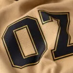 Custom baseball T-shirt number print close-up showing black-and-gold 07 graphic on textured tan fabric