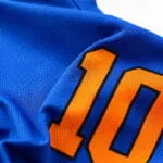 Breathable blue polyester mesh fabric close-up with sublimated orange number on custom baseball jersey