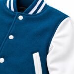 Close-up of topstitched white welt pocket trim, white snap buttons and blue and white striped rib cuff on a varsity jacket