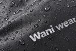 Close-up of water droplets beading on waterproof duffle bag fabric with printed Wani Wear logo