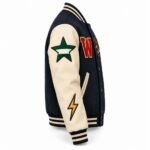 Side view of a navy and cream letterman jacket with a green star patch, gold lightning-bolt patch and striped rib cuffs