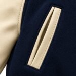 Close-up of a slanted welt pocket with cream trim and topstitching on navy jacket fabric