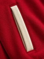 Close-up of red textured body fabric, cream twill sleeve and red-and-cream striped rib-knit collar on a varsity jacket