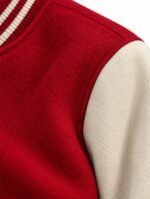 Close-up of a varsity jacket welt pocket with cream trim and red topstitching on textured red fabric