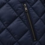 Close-up of metal zip welt pocket on navy diamond-quilted varsity jacket