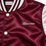 Close-up of white script embroidery, woven neck label and snap buttons on maroon satin jacket