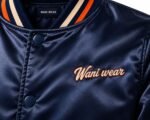 Close-up of embroidered script logo patch with orange outline and navy snaps on a satin jacket