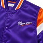Close-up of white script embroidery with orange swoosh and purple snaps on a satin team jacket